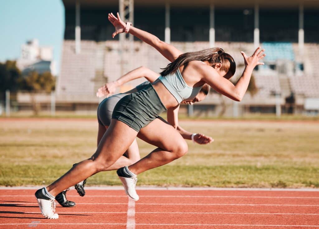 Zwei Sportlerinnen beim Start eines Leichtathletikrennens Sprinterinnen starten auf Tartanbahn | Medaille kaufen
