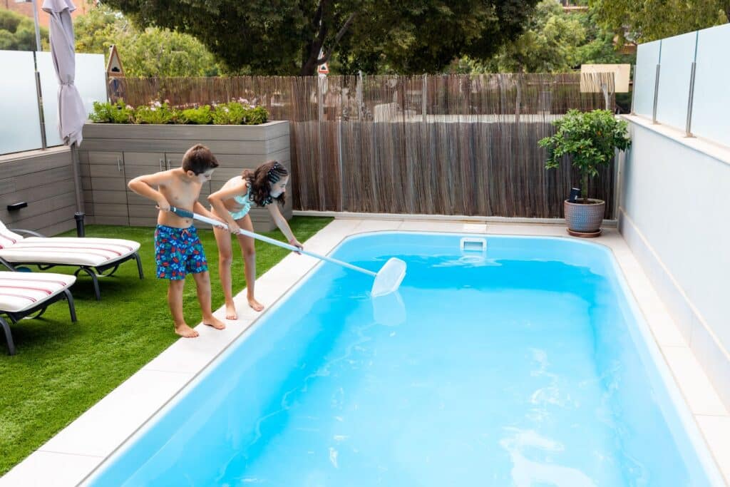 Zwei Kinder reinigen einen privaten Gartenpool mit einem Kescher – sichtbare Wasserpflege als Teil gesunder Poolnutzung